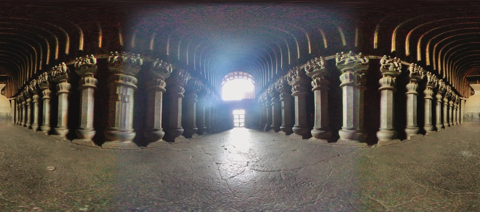 Photograph inside the Karla Caves chaitya hall: two rows of carved stone pillars leading to a stupa under a vaulted rock-cut roof.